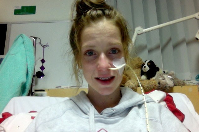 Grace Brandenburg sits in a hospital bed with a drip in her nose.