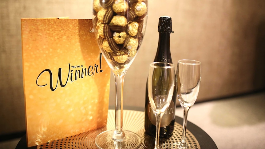 A gold booklet, a glass filled with chocolates and a bottle of champagne on a table.