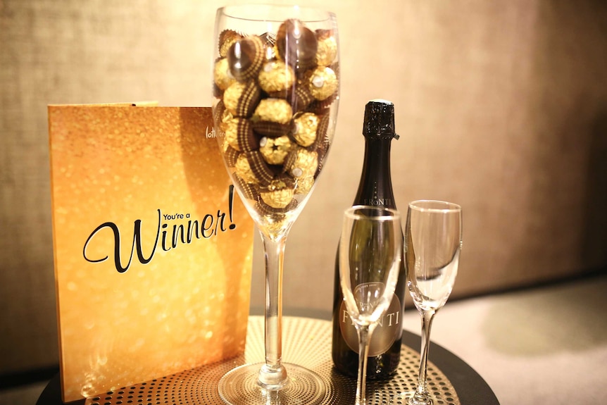 A gold booklet, a glass filled with chocolates and a bottle of champagne on a table.