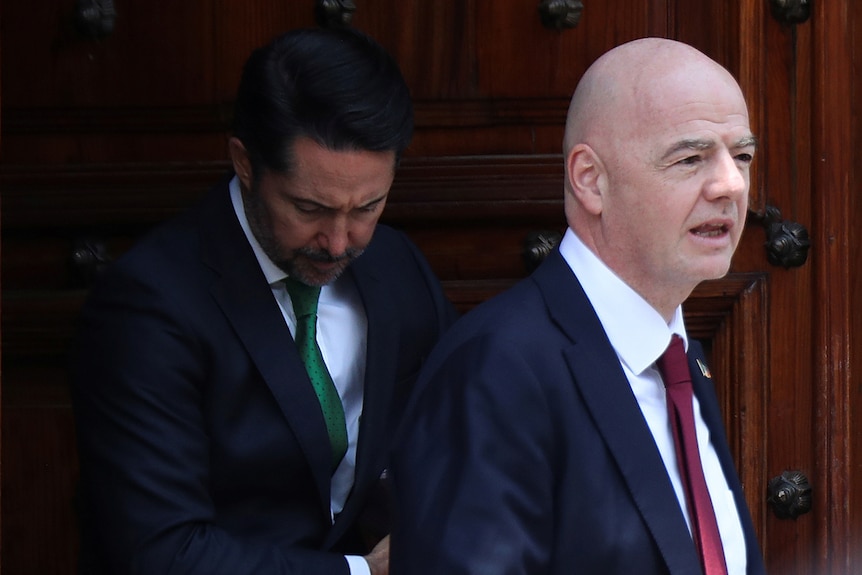 Gianni Infantino walks out of a doorway followed by the Mexican president. 