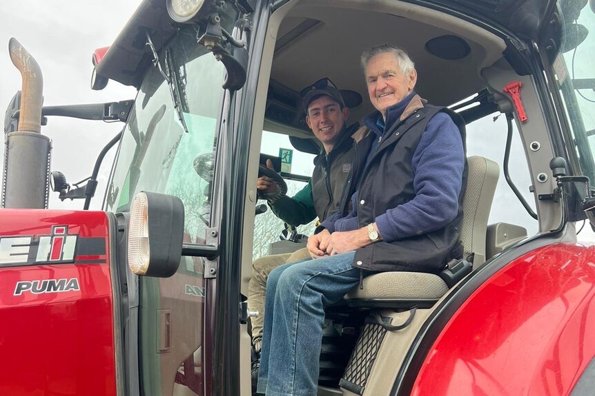 two men sit inside the cab of a red tractor