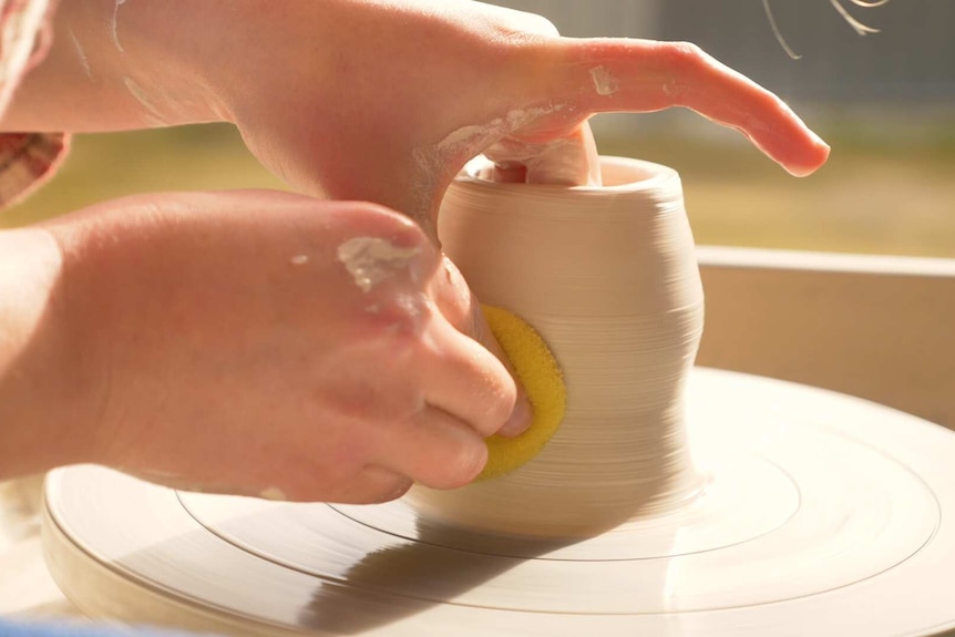 A young woman working on the pottery wheel at her studio.