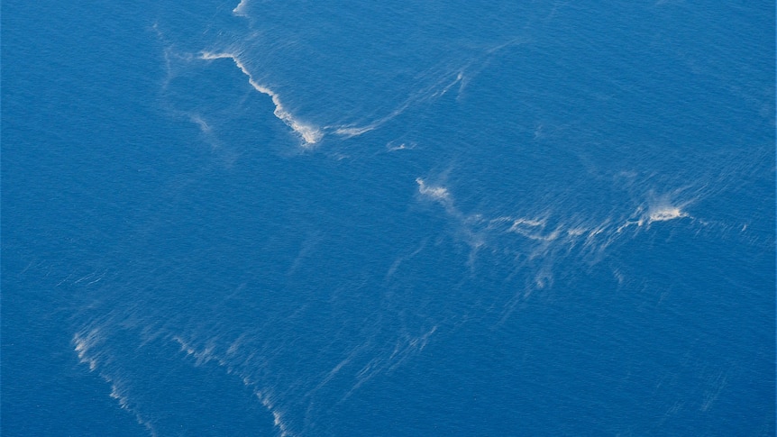 Oil slicks are seen in the ocean from an aerial view.