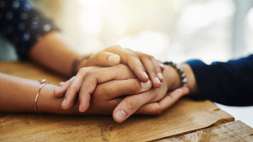 A person's two hands are wrapped around another person's hand, in a close up shot.