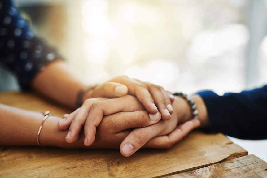 A person's two hands are wrapped around another person's hand, in a close up shot.