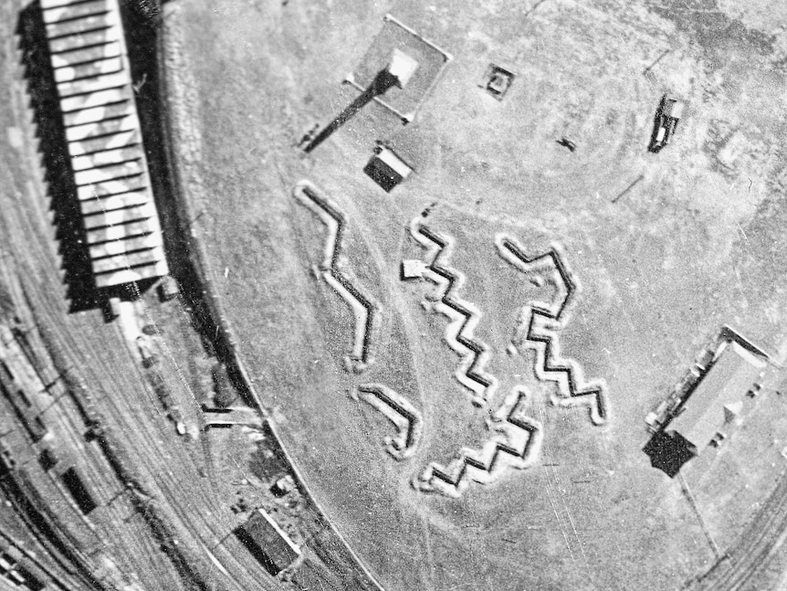 A black and white aerial photo on a field with buildings and zig zag shaped trenches