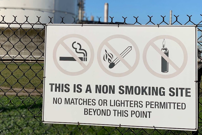 An industrial storage tank with a "no smoking sign" in front of it.