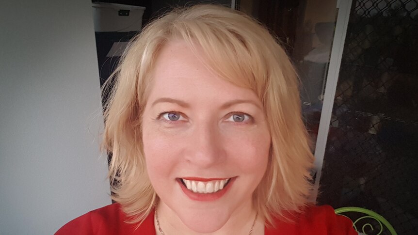 Portrait of a woman with shoulder length blond hair in a red dress, smiling at camera.