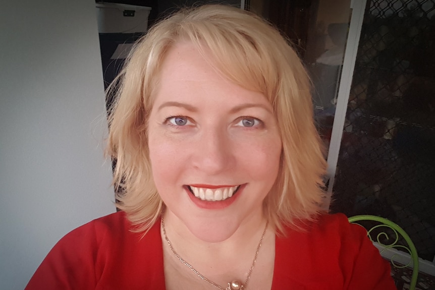 Portrait of a woman with shoulder length blond hair in a red dress, smiling at camera.