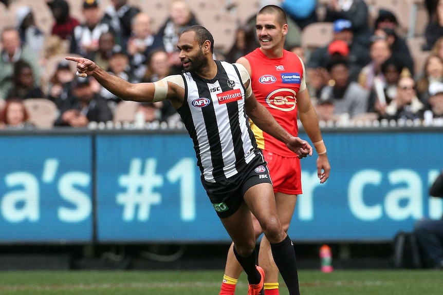 An AFL player points in triumph after kicking a goal.