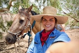 A young woman wearing a straw hat with horse behind her