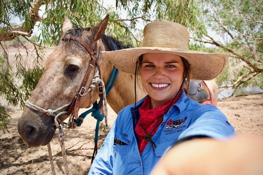 A young woman wearing a straw hat with horse behind her