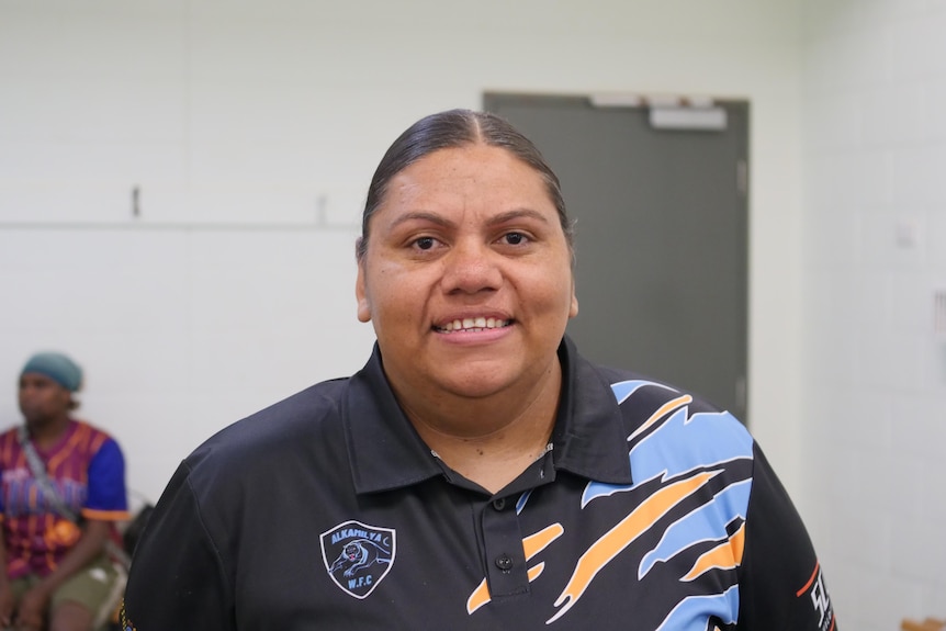 Danni Woods smiles at the camera in the change rooms of her football club.