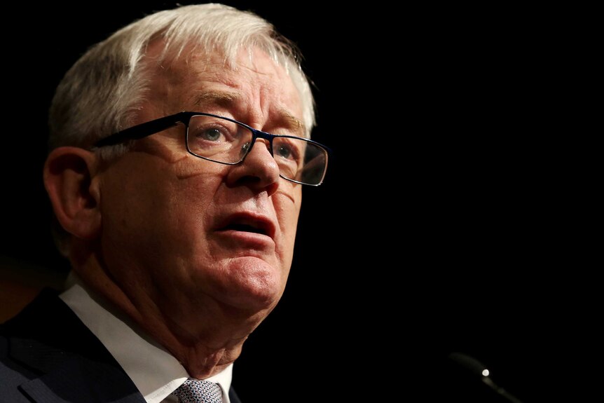 Andrew Robb stands in front of a black background.