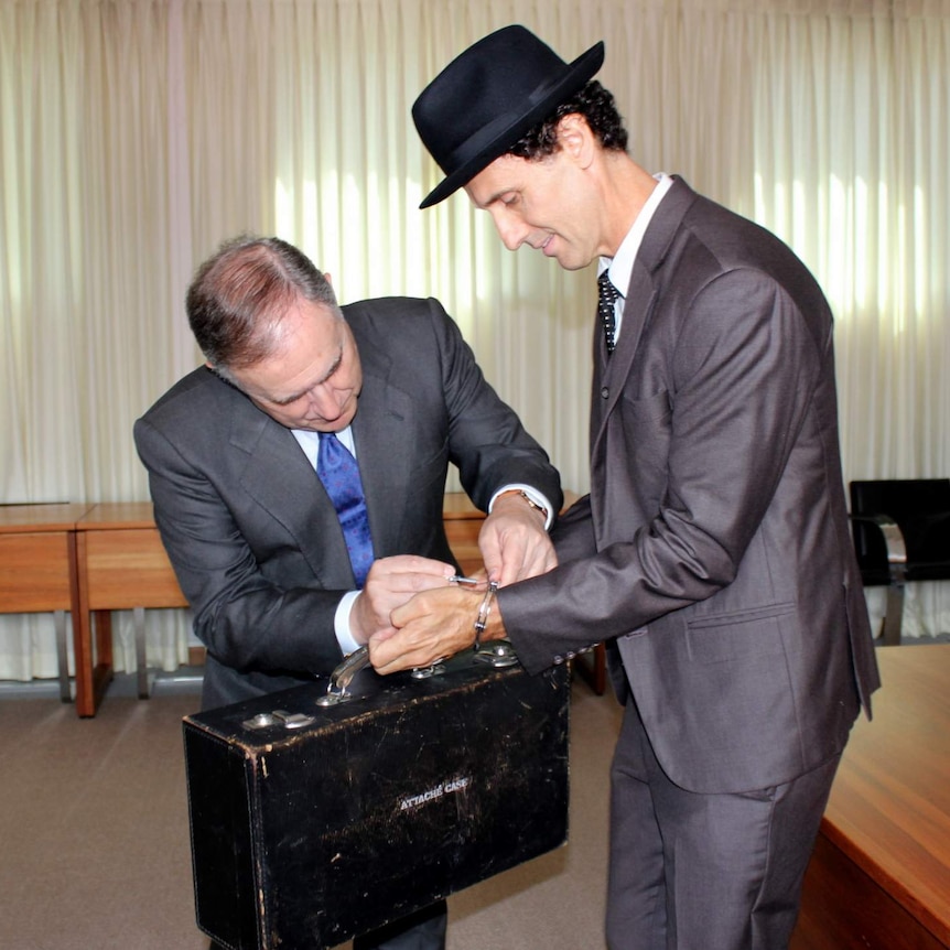 Spanish ambassador Enrique Viguera unlocks the briefcase handcuffed to to the wrist of artist Peter Burke.