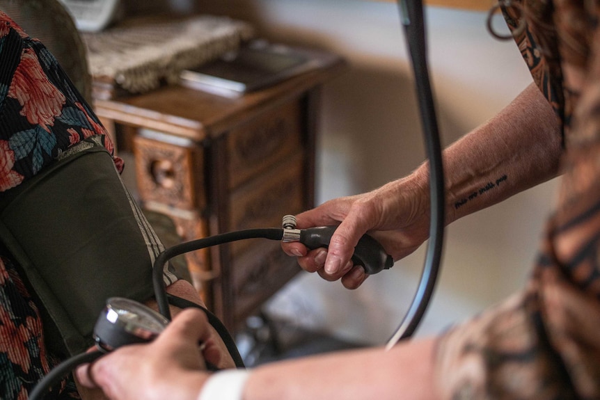 A close up shot of an elderly patients blood pressure being taken, a hand with a tattoo on the arm takes it.