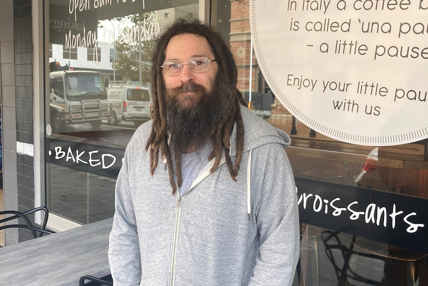 a man with dreadlocks stands and smiles in front of a store
