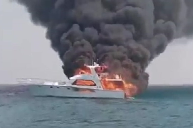 A boat on fire with a large, dark plume of smoke spewing out of it.