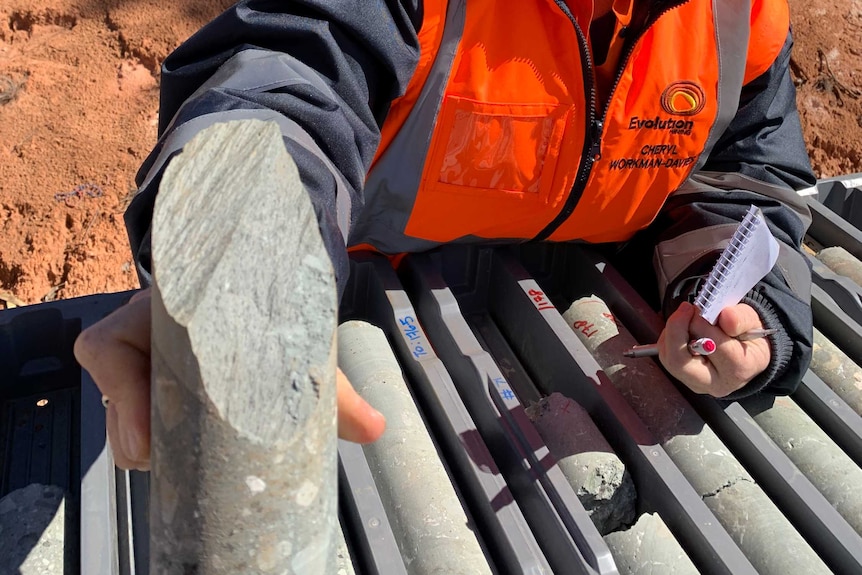 A woman wearing high-vis workwear holding drilling samples.