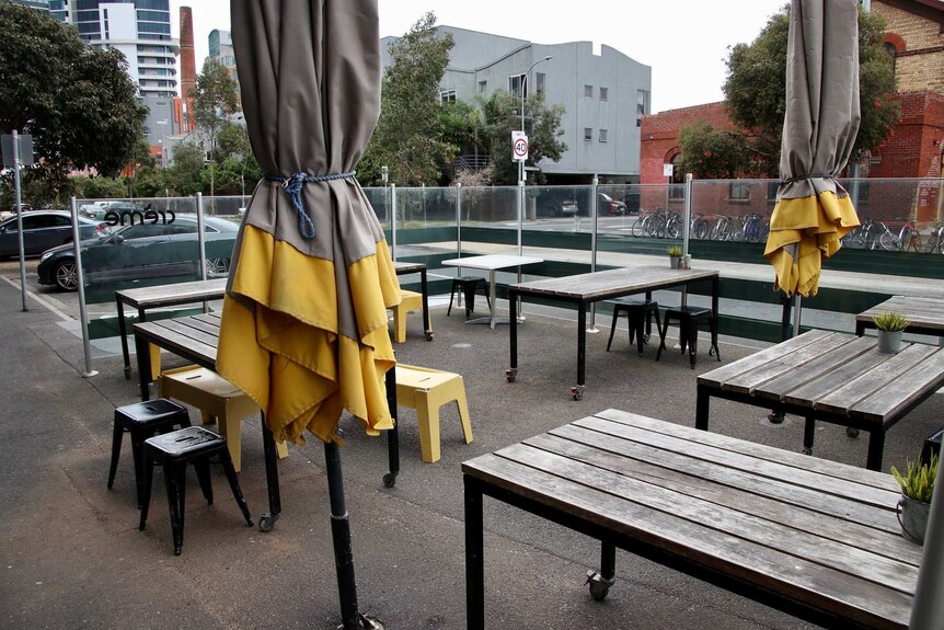 Empty tables outside a cafe with closed umbrellas next to them on a grey day.