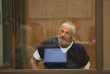 Nick Philippoussis sits behind a glass screen in court.