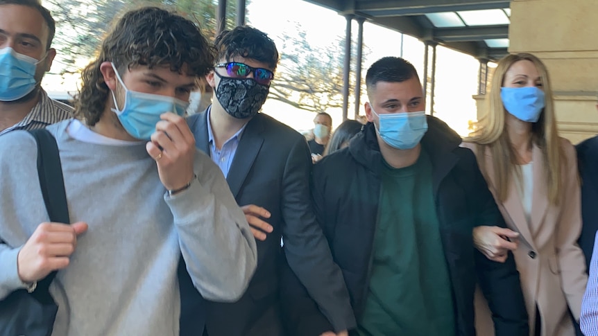 A group of five people wearing masks walk towards cameras outside court