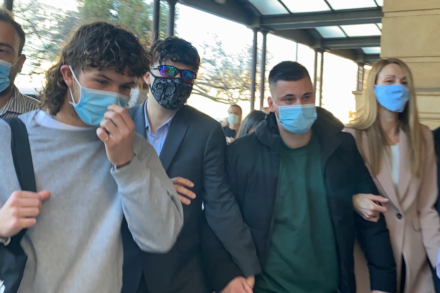 A group of five people wearing masks walk towards cameras outside court