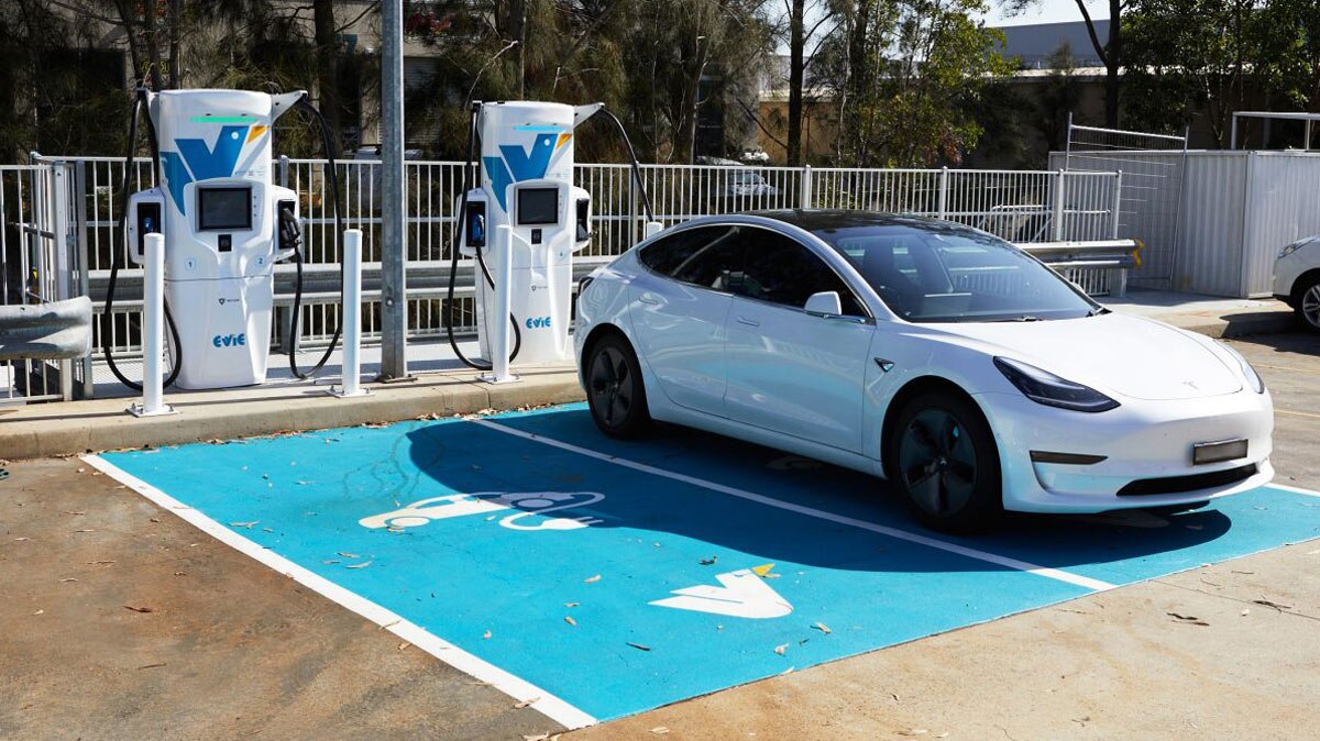 A car parked in a blue parking bay beside EV charger stand