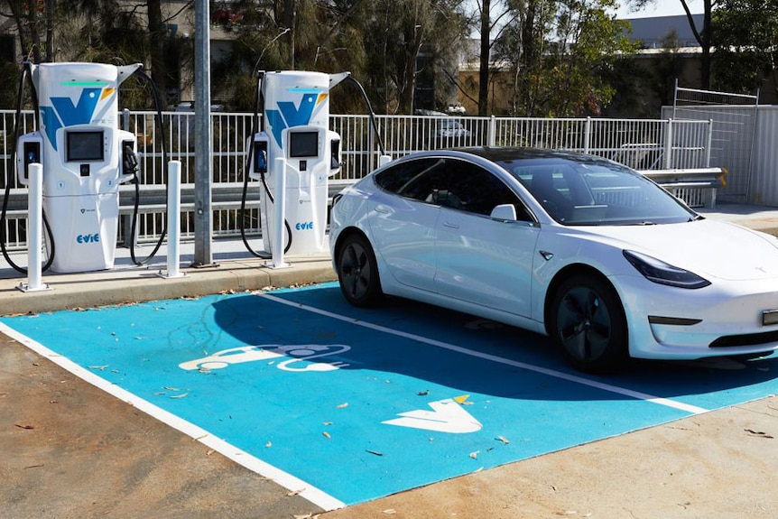 A car parked in a blue parking bay beside EV charger stand