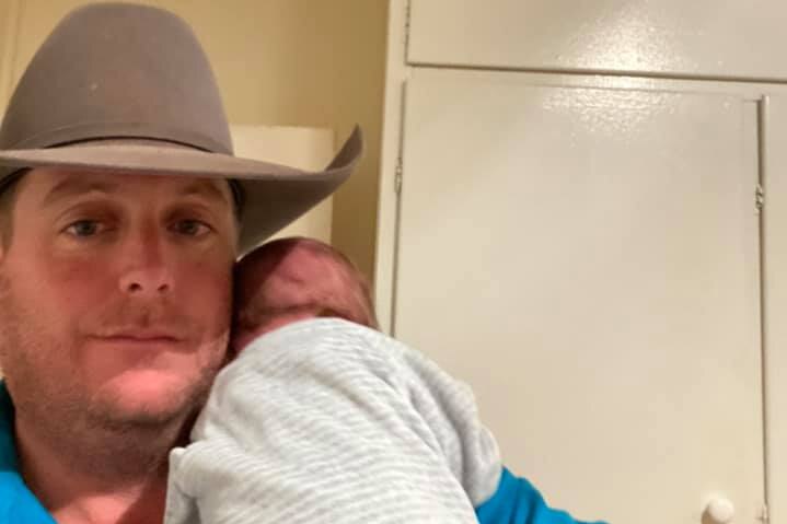 A fatherin cowboy hat nurses newborn baby.