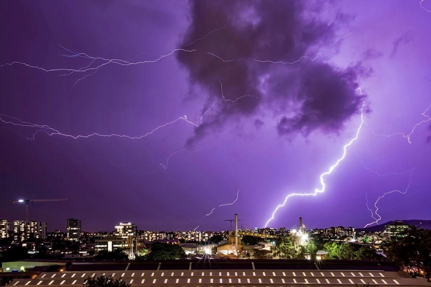 Lightning strikes in night time purple skies above Brisbane suburbs.