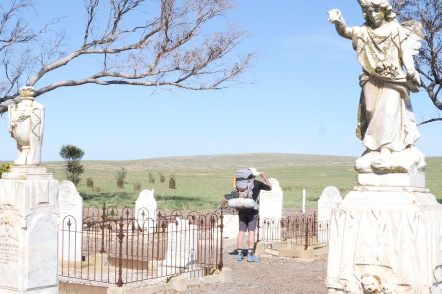 Wide shot of old cemetery, man with back to camera tipping hat at grave site in distance