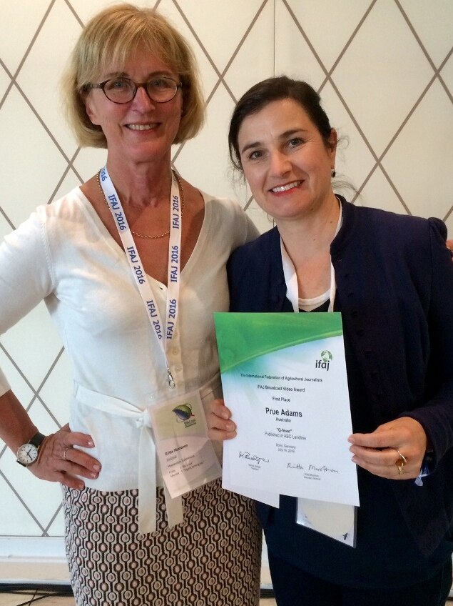 Two women stand together, one holding an A4-sized certificate of award