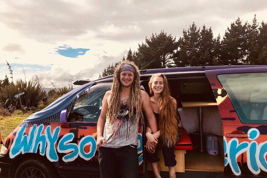 Mike Perman and Aubry Lewis in front of a camper van, they are holding hands and smiling.