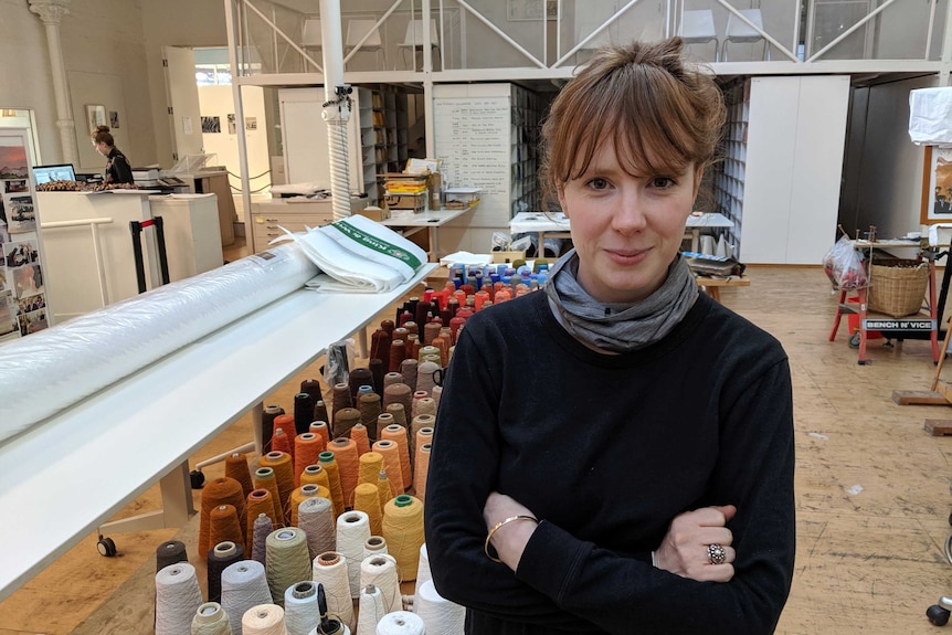 A woman poses for the camera in front of colourful looms of material