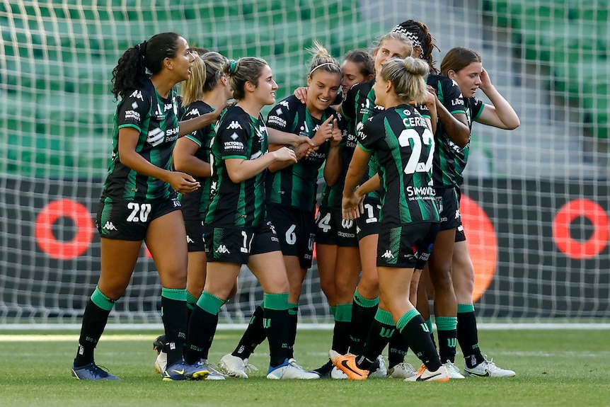 A group of soccer players wearing green and black uniforms gather in a crowd to celebrate during a match