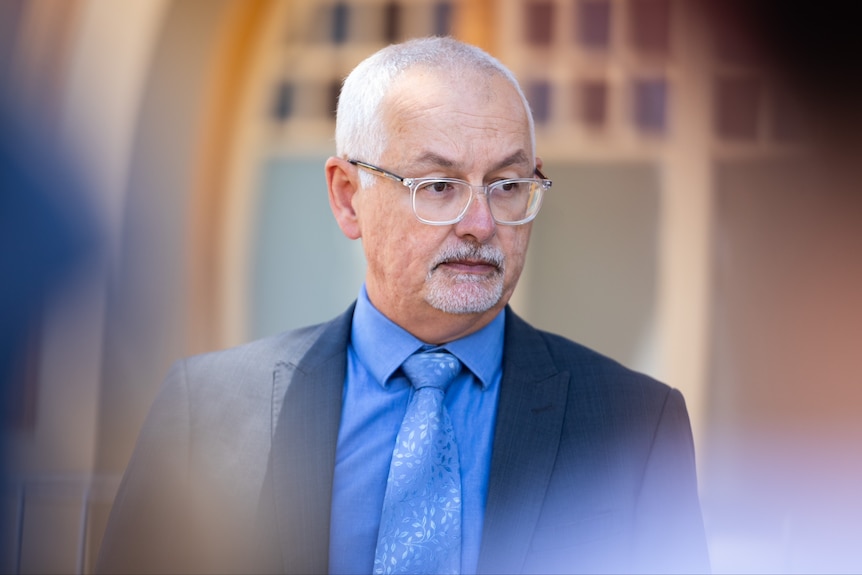 A man wears a blue suit and glasses