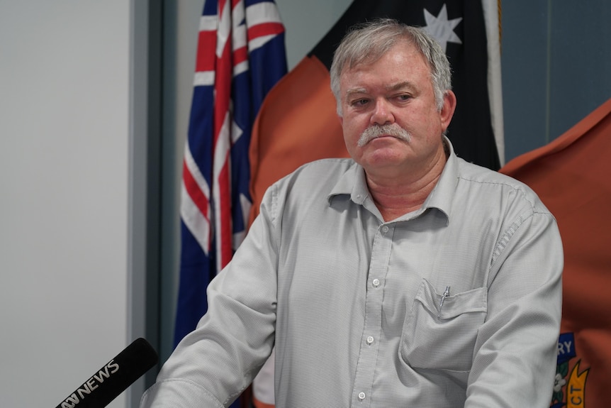 A man with a moustache in a grey shirt looks off to his left.