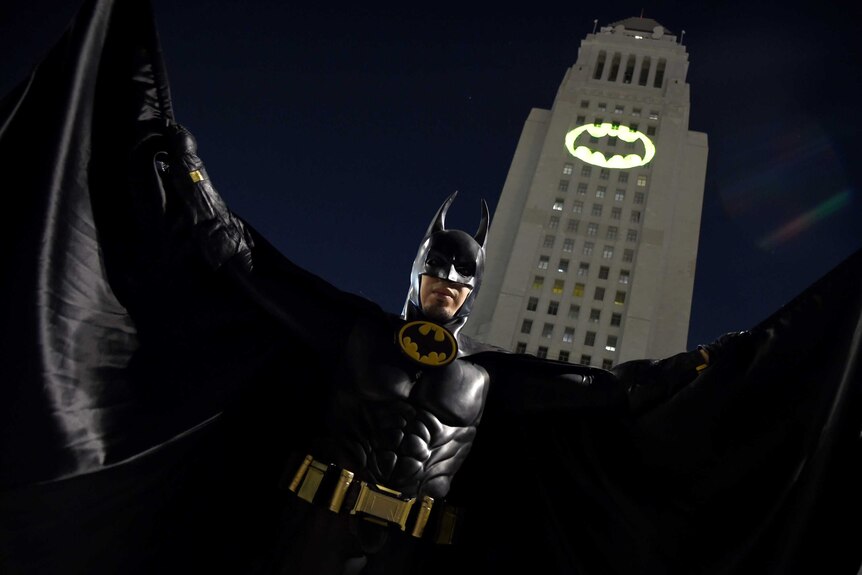 A man dressed as Batman poses in front of a Bat-Signal projected onto City Hall in Los Angeles.