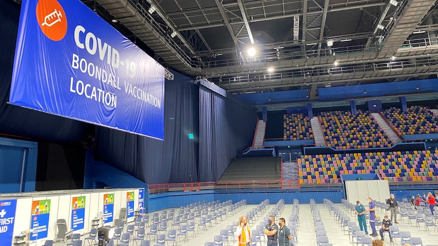 A large auditorium with a sign reading "COVID-19 Boondall Vaccination Location".