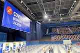 A large auditorium with a sign reading "COVID-19 Boondall Vaccination Location".