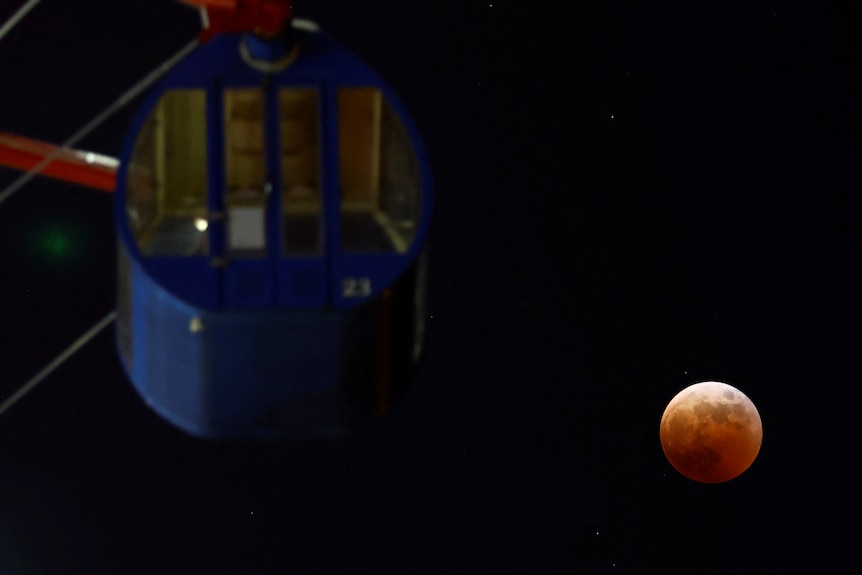The moon and a Ferris wheel at a park are seen during a lunar eclipse in Tokyo, Japan