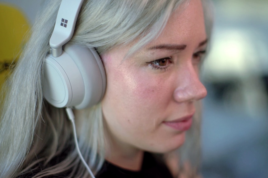 A close up shot of a woman's face from the side. She's wearing over-ear headphones.