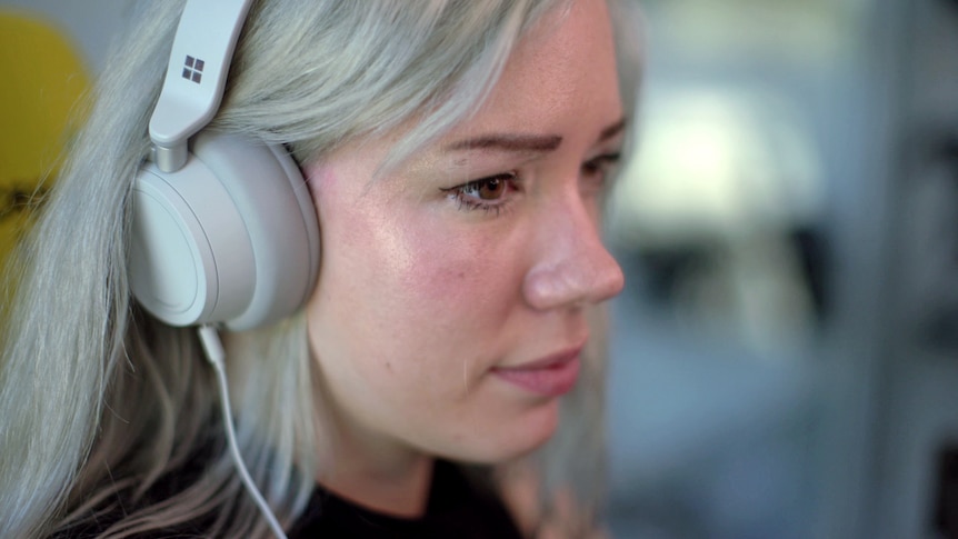 A close up shot of a woman's face from the side. She's wearing over-ear headphones.