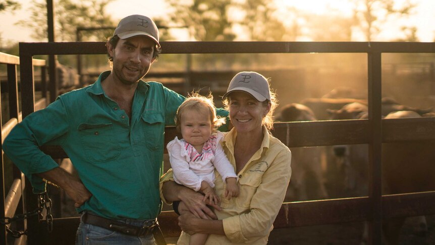 Husband, wife and baby child in front of their farm fence in Northern Territory cattle yard.