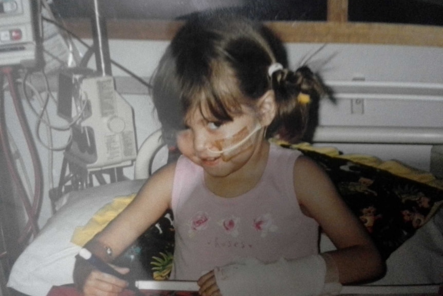 A child sits in a hospital bed with a tube on her face