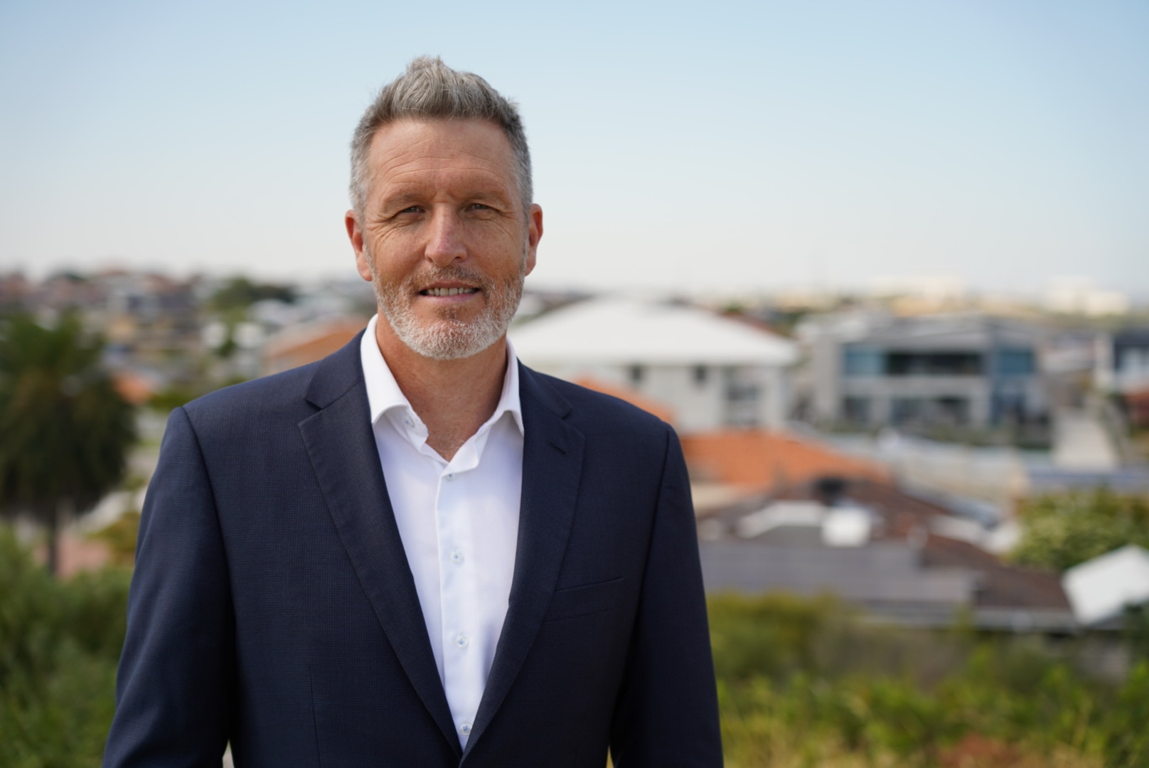 Josh Wilson stands smiling wearing a jacket and shirt. 