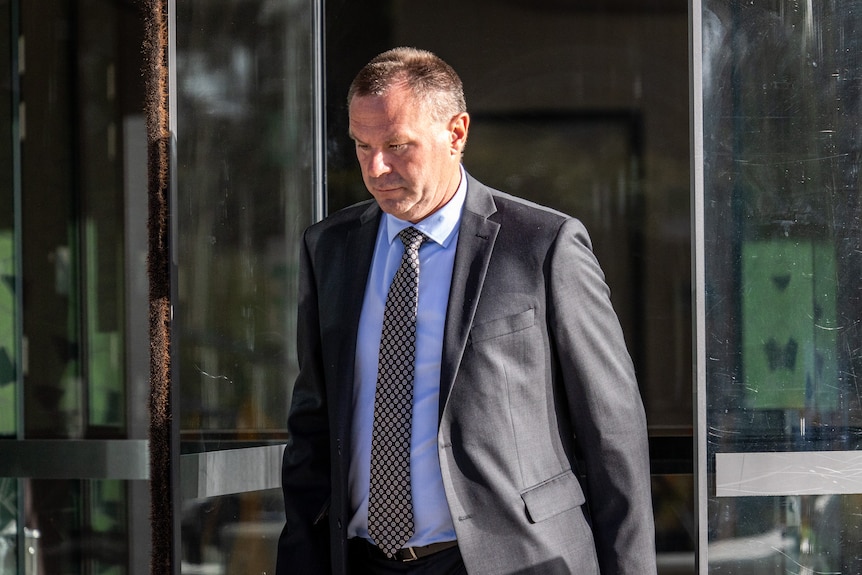 A man wearing a suit and tie walks with his eyes down