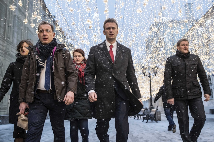 Alexei Navalny walks on the street, through the snow, and others walk beside him.