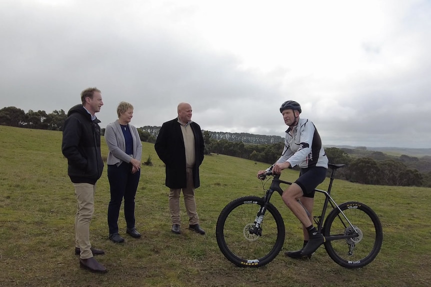 Three people standing and a man with a bike on a hill
